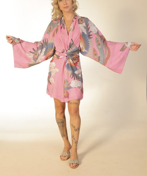 Mulher loira usando um vestido curto manga longa amarração na cintura estampa exclusiva pavão pink praticidade leveza conforto elegância maria sanz kimono quimono