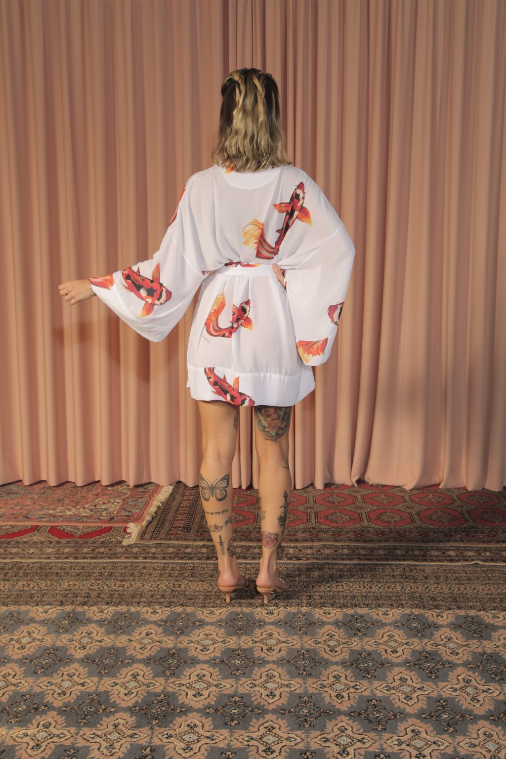 Mulher loira usando um kimono curto manga longa faixa na cintura estampa exclusiva de branco com carpas terceira peça leveza conforto praticidade maria sanz kimono quimono