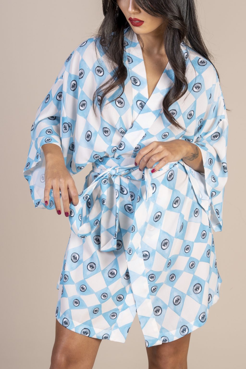 Mulher morena usando um kimono curto manga curta estampa exclusiva losango bege e azul com olhos desenhados a mão joker conforto praticidade elegância maria sanz kimono quimono