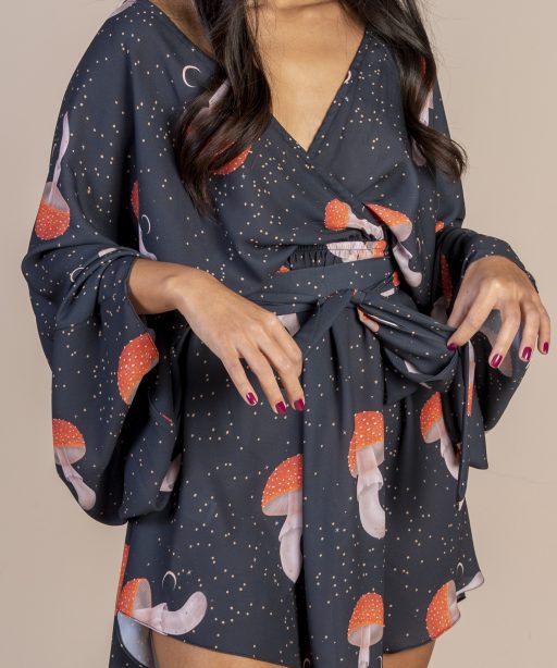 Mulher morena usando um vestido curto manga curta decote v com elástico e faixa na cintura estampa exclusiva preto cogumelos desenhados a mão praticidade elegância conforto maria sanz kimono quimono