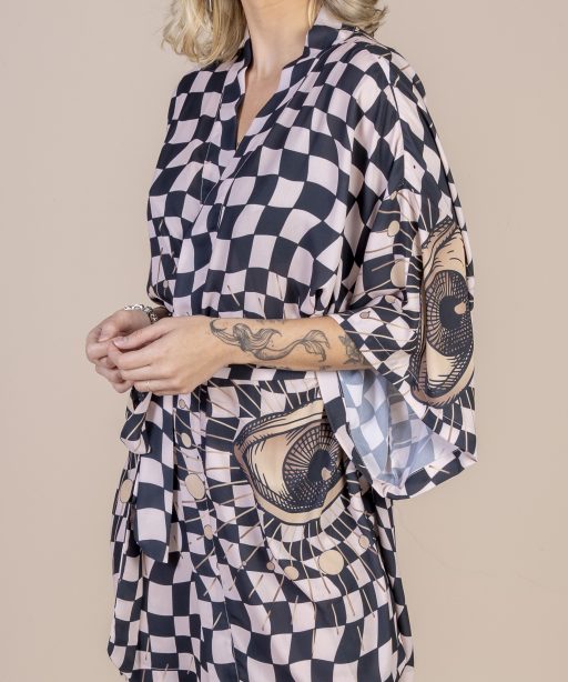 Mulher loira usando um kimono curto manga curta estampa exclusiva xadrez preto e bege com olhos grandes desenhados a mão conforto faixa para amarração na cintura praticidade elegância maria sanz kimnono quimono