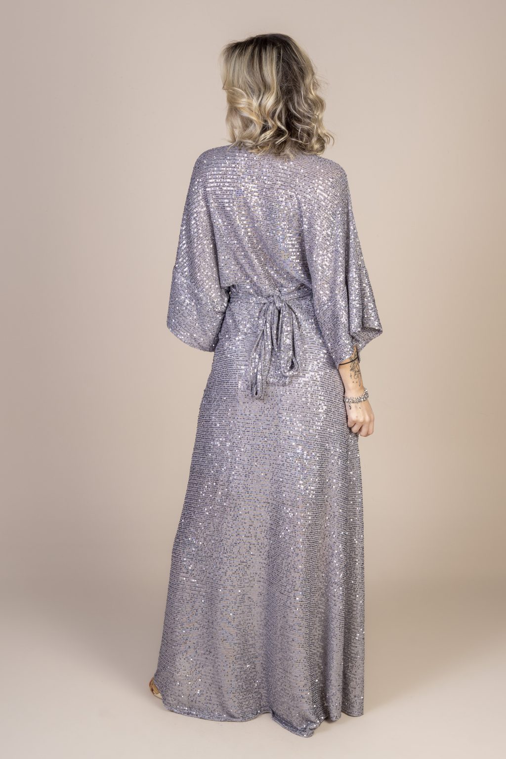Mulher loira usando um vestido longo manga curta paetê prata brilhoso com amarração na cintura conforto praticidade elegância festa joker maria sanz kimono quimono